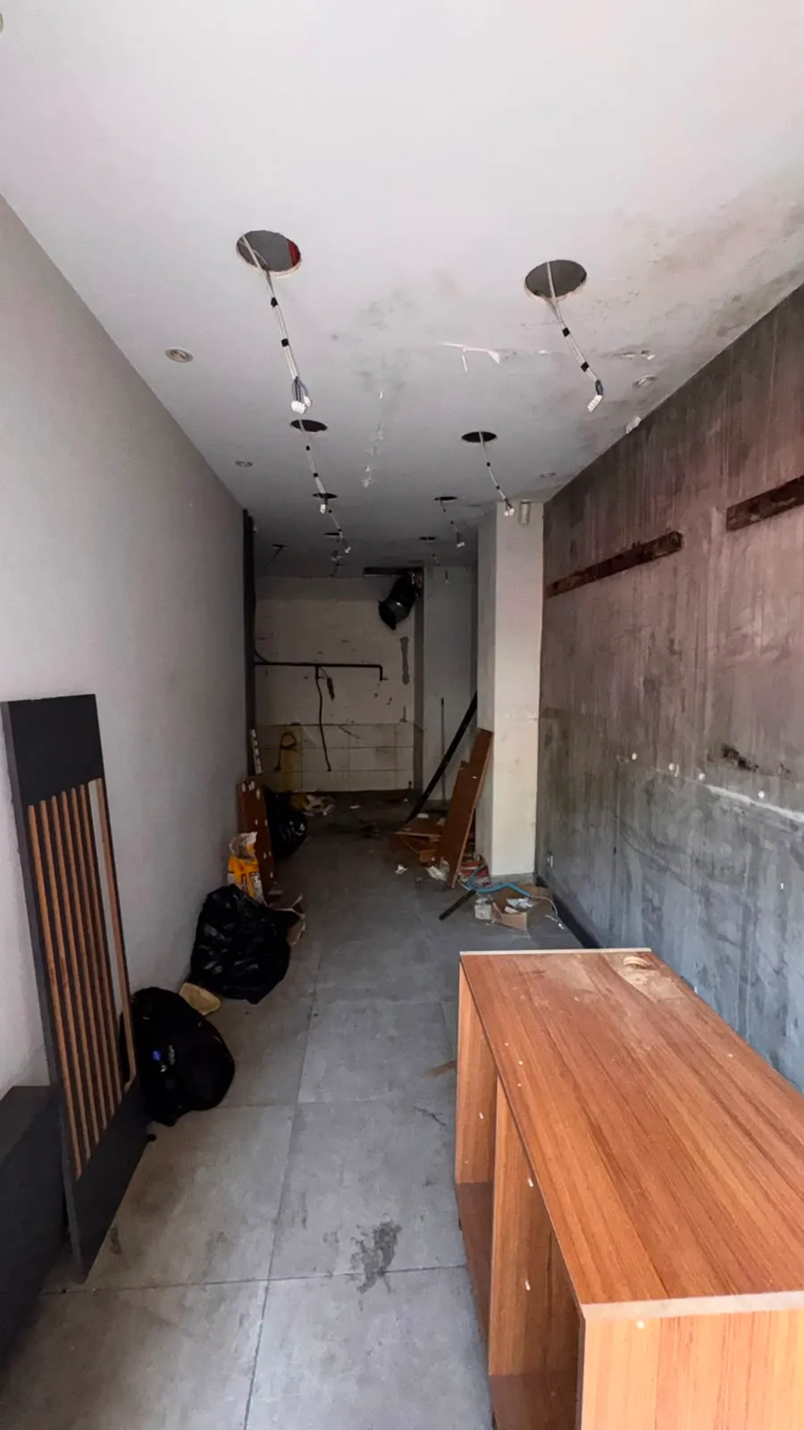 Giriş katının arka bölümünden sokağa doğru uzanan boş ticari alan ve tavandaki aydınlatma noktaları.